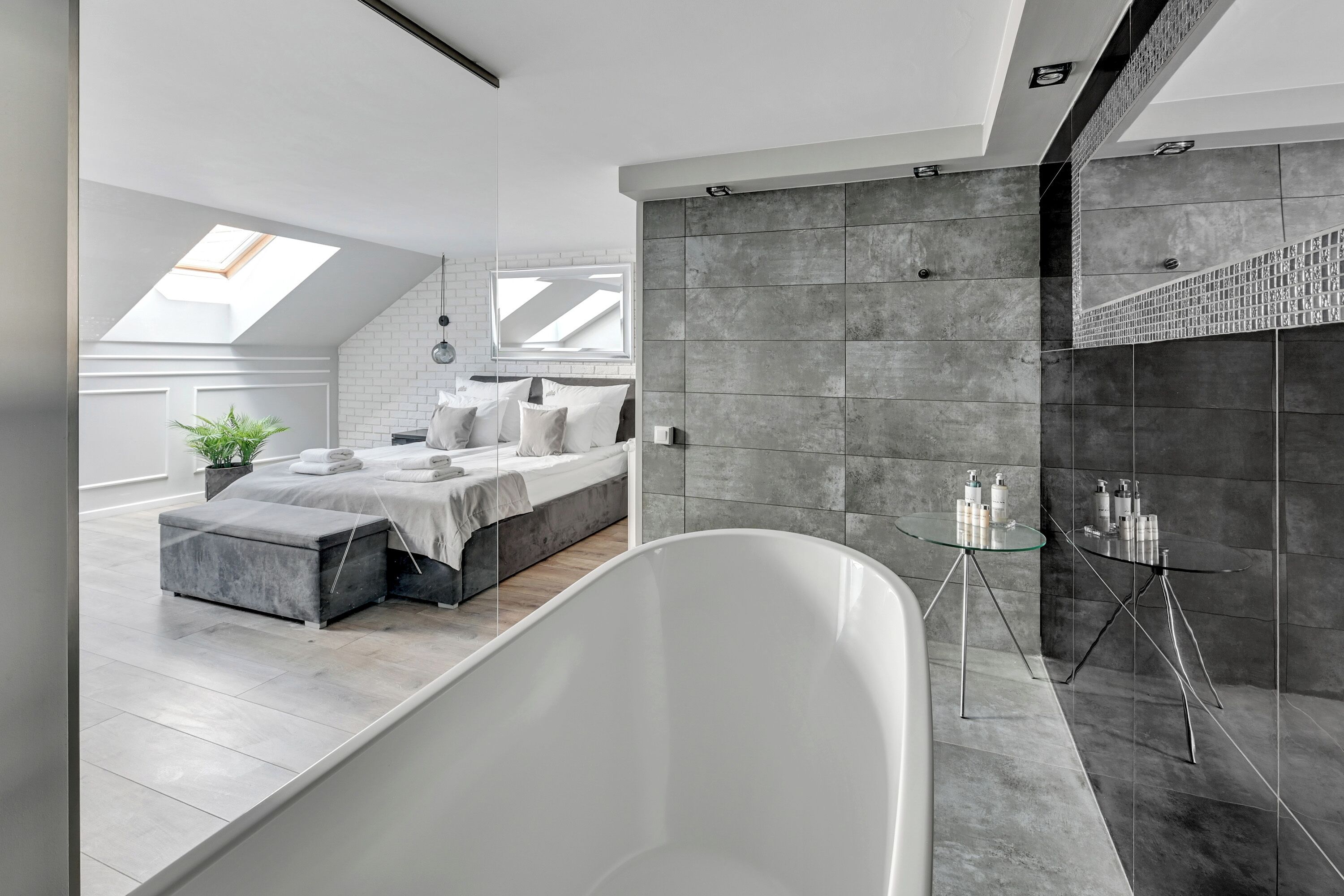 A modern bedroom with a skylight, a large bed, and a freestanding bathtub.