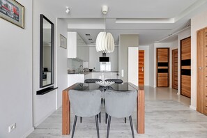 A modern dining area with a glass table and two grey chairs, a pendant light, and wooden doors in the background. - Waterlane Riverside SPA, Pool & Gym by Downtown Apartments (Gdansk)