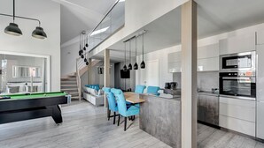 Een moderne keuken met een ingebouwde oven en magnetron, een eetgedeelte met blauwe stoelen en een pooltafel.