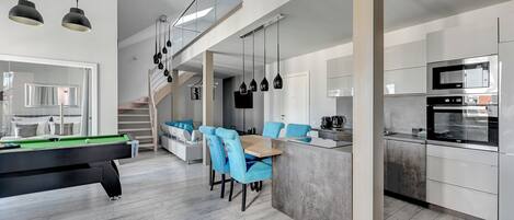 A modern kitchen with a built-in oven and microwave, a dining area with blue chairs, and a pool table.