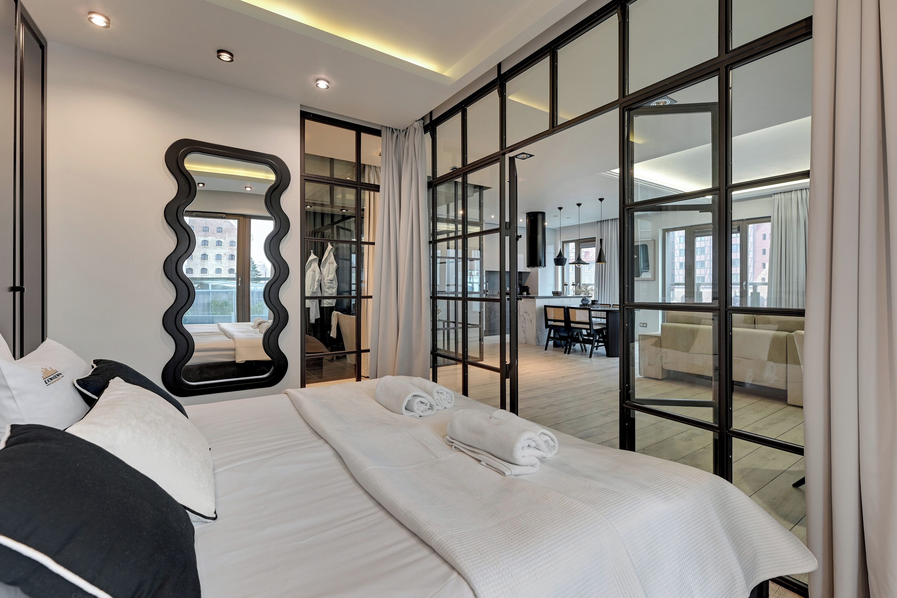 A hotel room with a large bed, a mirror, and a view of the dining area.