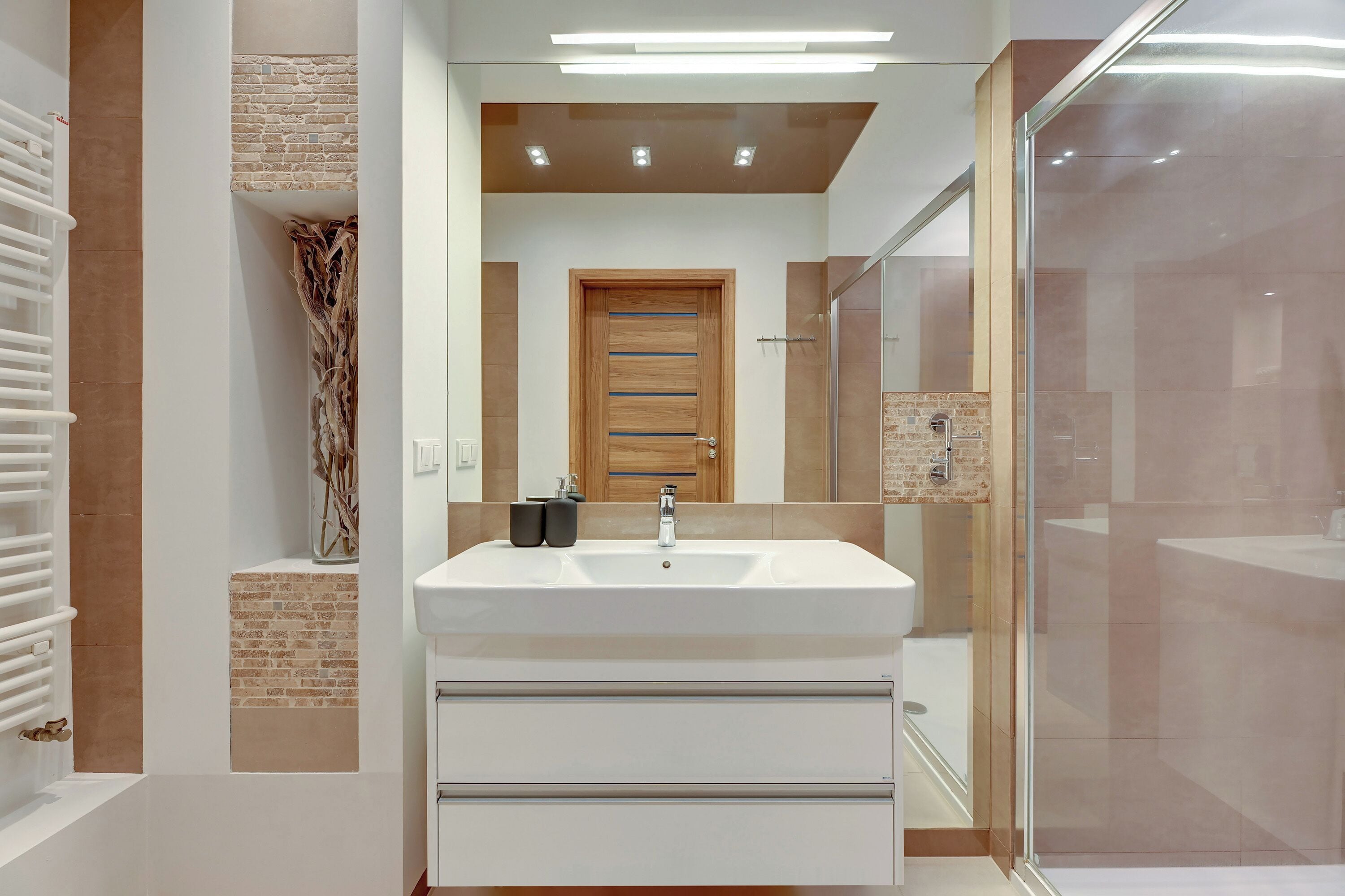 A modern bathroom with a large sink, a glass shower enclosure, and a wooden door.