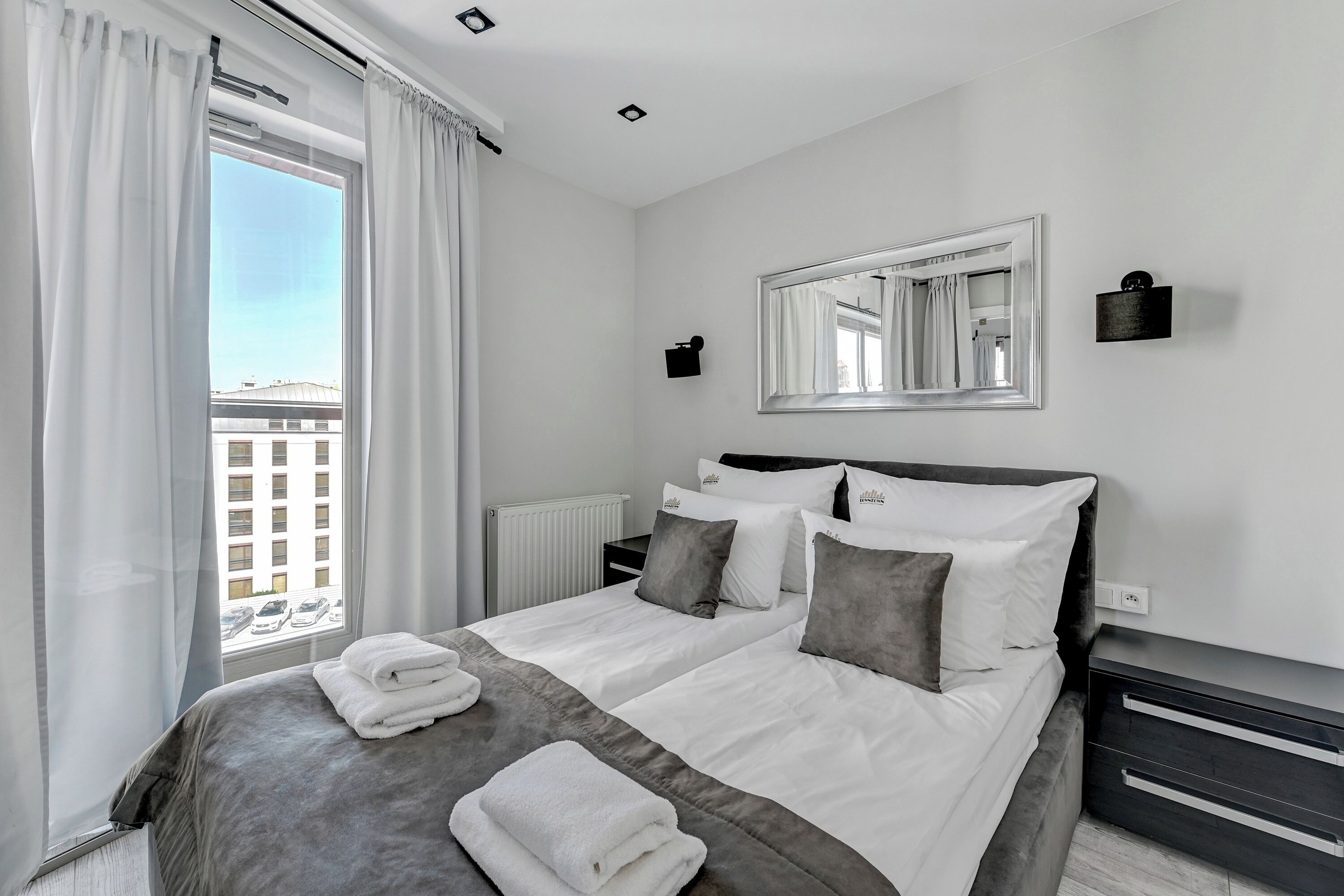 Una camera d'albergo moderna con un letto grande, un comodino, uno specchio e vista sulla città dalla finestra.