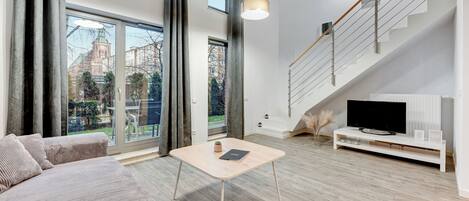 Una sala de estar moderna con un sofá, una mesa de centro, un televisor sobre un soporte blanco y una escalera.