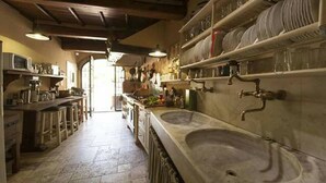 A kitchen with a large sink, shelves with dishes, and a view into another room. - Villa Gabriella Chianti Toscana (Città Metropolitana di Firenze)