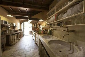 A kitchen with a large sink, shelves with dishes, and a view into another room. - Villa Gabriella Chianti Toscana (Città Metropolitana di Firenze)