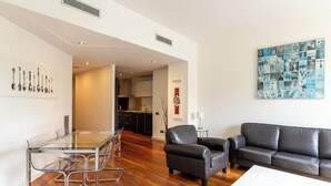A modern living room with a glass dining table, leather sofa, and a wall art piece.