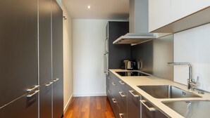 A modern kitchen with dark cabinetry, stainless steel appliances, and a wooden floor.