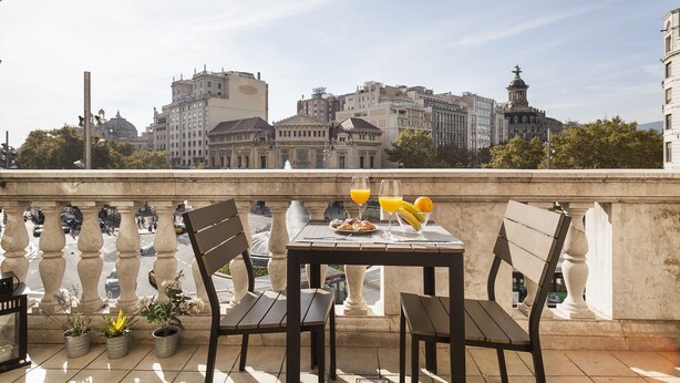 A balcony with a table set for breakfast, potted plants, and a view of city buildings.
