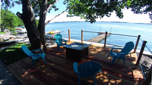 Une terrasse en bois avec des sièges d’extérieur, un foyer et une vue sur un lac.