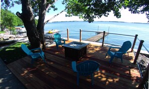 A wooden deck with outdoor seating, a fire pit, and a view of a lake. - Beautifully Remodeled Lake Front Home ~ Includes Kayaks!   (Lake City)