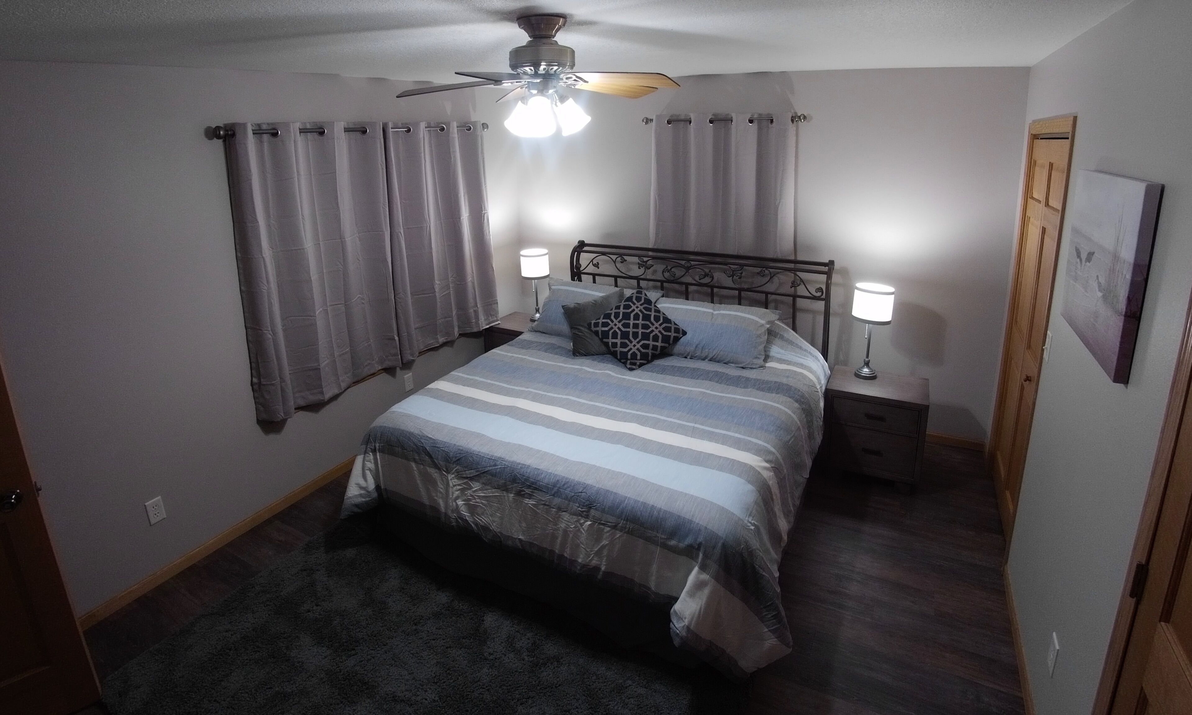 Ein Schlafzimmer mit einem Bett, zwei Nachttischen, einem Deckenventilator und einem Beistelltisch mit Lampe.