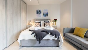 A modern bedroom with a large bed, grey bedding, a grey sofa, and two wall-mounted paintings.
