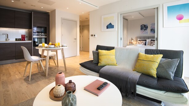 A modern living room with a sofa, a dining table, and a kitchen area.
