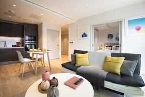 A modern living room with a sofa, a dining table, and a kitchen area. - The Kings Cross flat by City Apartments UK (London)