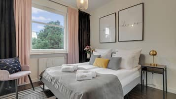Habitación de hotel con cama, una silla, mesita de noche, lámpara y ventana con cortinas.