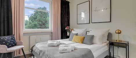 Ein Hotelzimmer mit Bett, Sessel, Nachttisch, Lampe und einem Fenster mit Vorhängen.