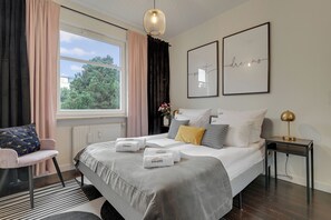 A hotel room with a bed, a chair, a bedside table, a lamp, and a window with curtains. - Sopot Łokietka by Downtown Apartments (Sopot)