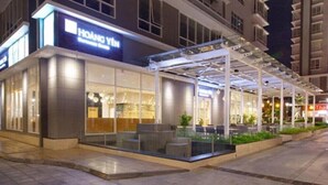 A hotel with a glass facade, outdoor seating area, and a covered walkway. - Enjoy Saigon Sunrise City (Ho Chi Minh City)