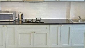 A kitchen with white cabinets, a microwave, a kettle, and a gas stove. - Enjoy Saigon Sunrise City (Ho Chi Minh City)