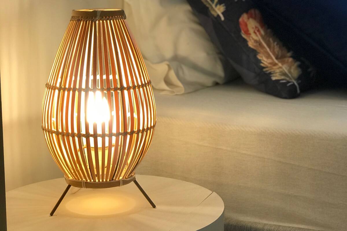 Ein runder Tisch mit einer modernen Lampe, platziert auf einem Bett mit Kissen und einer Decke.