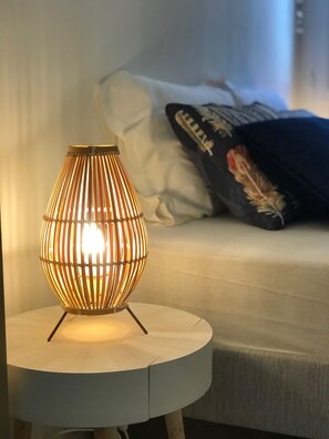 Une table ronde sur laquelle est posée une lampe moderne, le tout placé sur un lit agrémenté de coussins et d’une couverture.