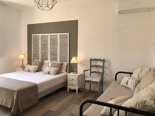 Une chambre à coucher comprenant un lit, deux tables de chevet, une chaise et un climatiseur fixé au mur.