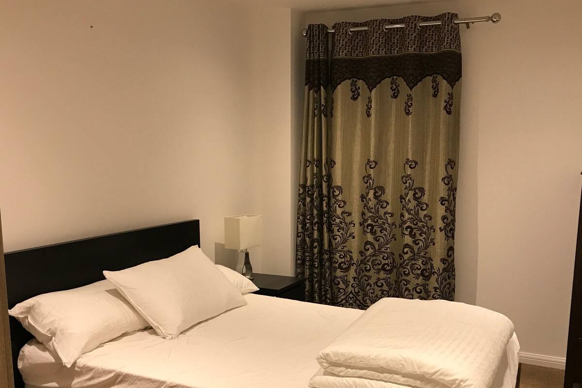 A neatly made bed with white linens in a room with a dark headboard.