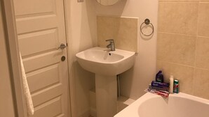 Ein Badezimmer mit einer weißen Tür, einem Standwaschbecken, einem Spiegel, einer Badewanne und Pflegeprodukten am Rand.