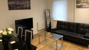 Ein modernes Wohnzimmer mit einem schwarzen Ledersofa, einem Glastisch, einem Flachbildfernseher, einem großen Spiegel und einem Stadtbild.