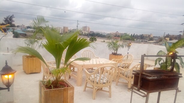 A rooftop terrace with a wooden table and chairs, surrounded by potted plants. - One World Apartments Bamburi (Mombasa)