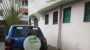 A blue car parked in front of a building with green window frames and a white exterior. - One World Apartments Bamburi (Mombasa)