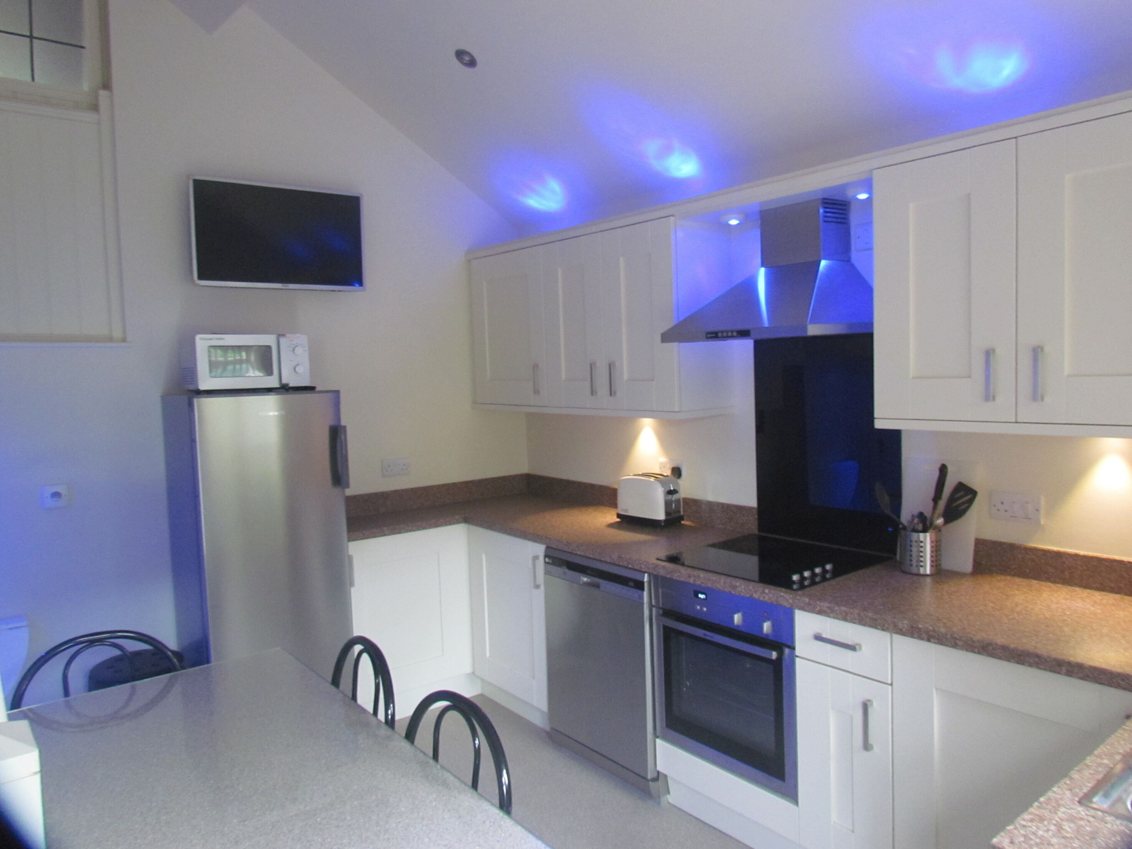 A modern kitchen with white cabinets, stainless steel appliances, and blue under-cabinet lighting.