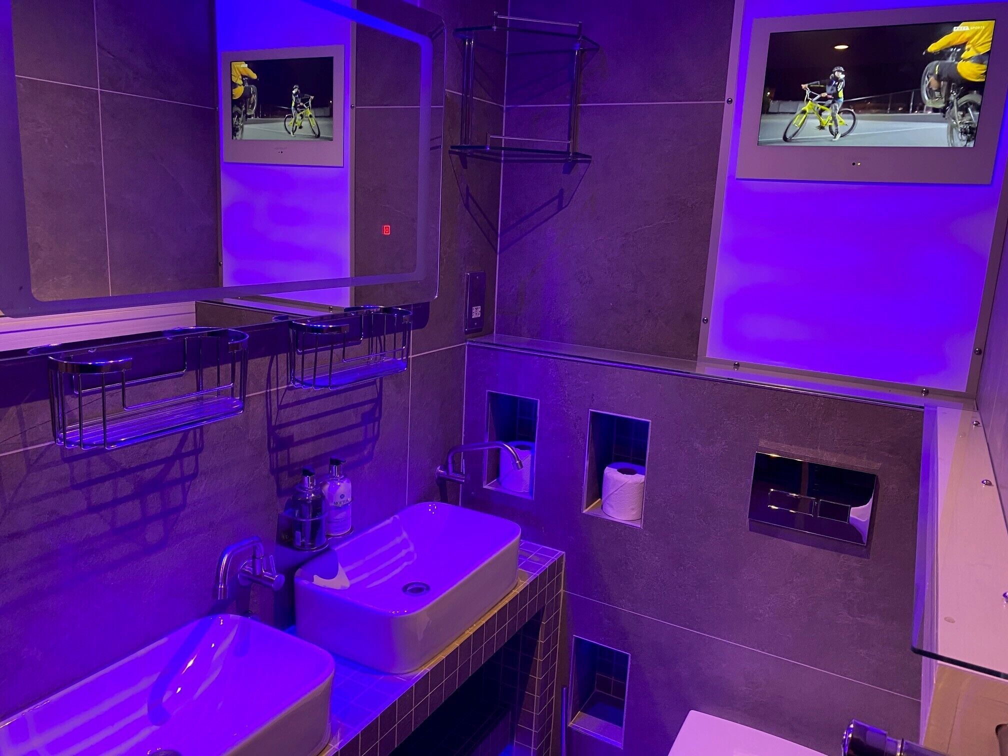 Un baño moderno con un espejo grande, dos lavamanos, un perchero para toallas y un inodoro.