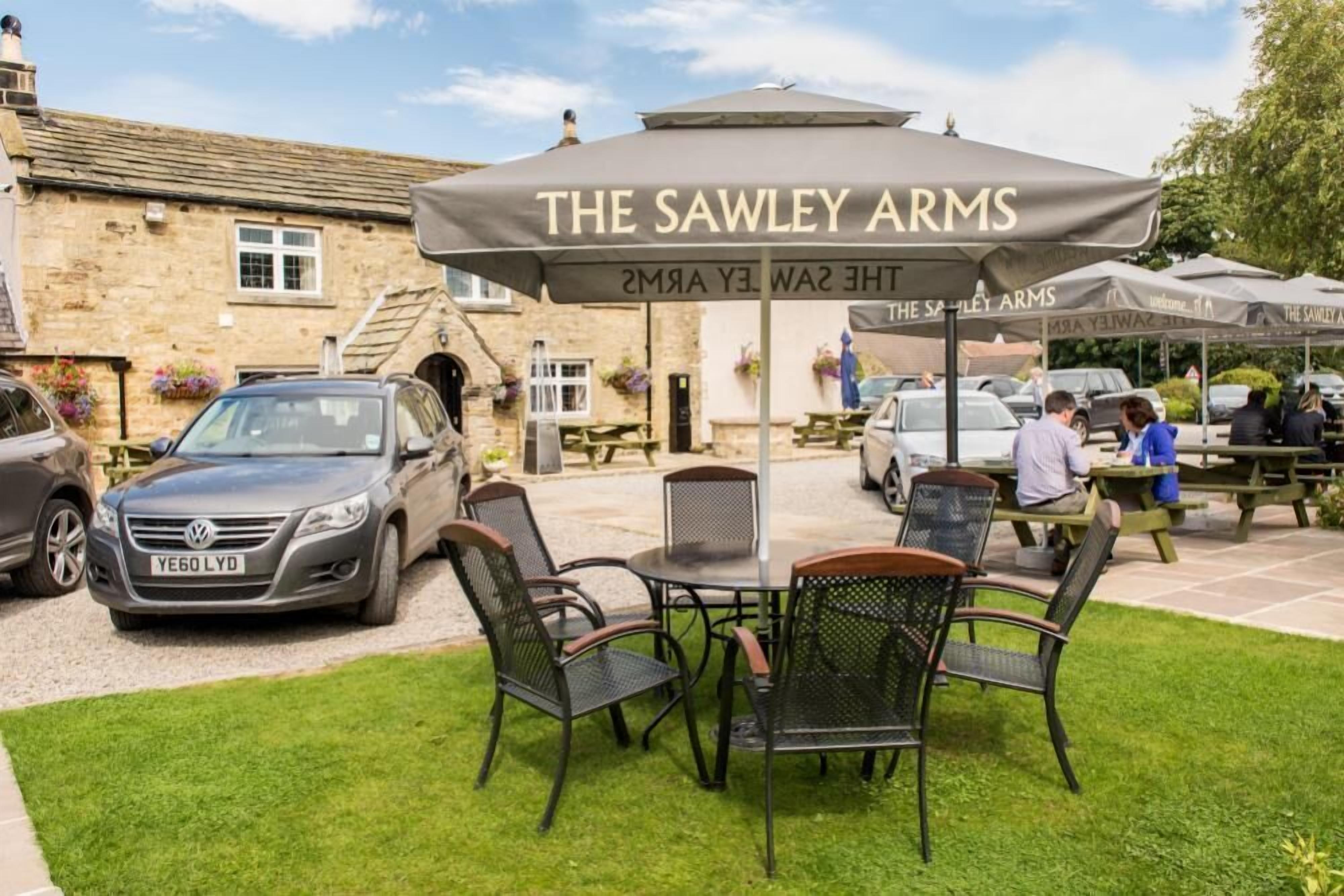 An outdoor seating area with a table and chairs under a branded umbrella at The Sawley Arms.