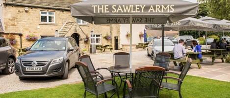 An outdoor seating area with a table and chairs under a branded umbrella at The Sawley Arms.