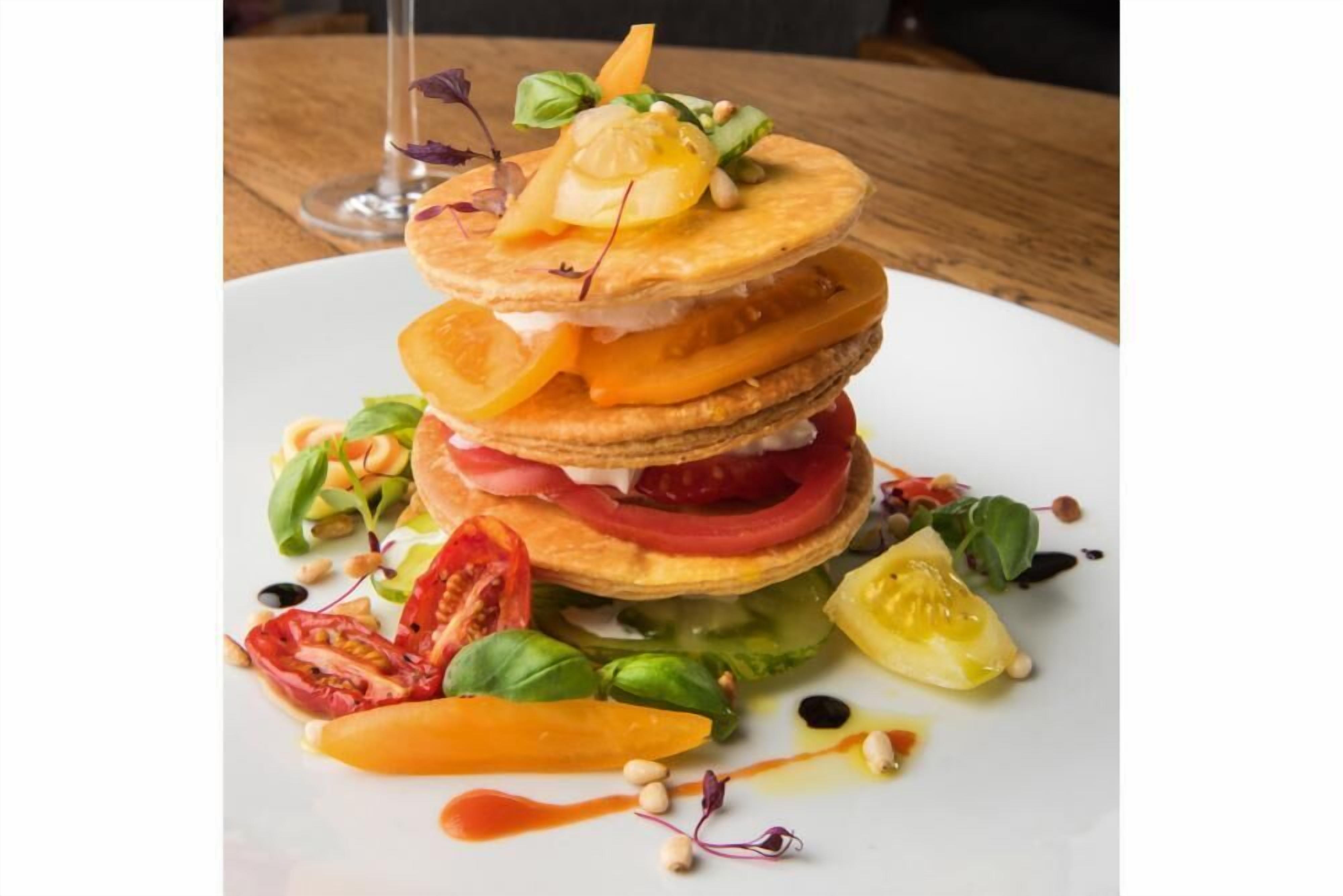 Una pila de tortitas con diferentes ingredientes y una ensalada al lado, sobre un plato blanco.