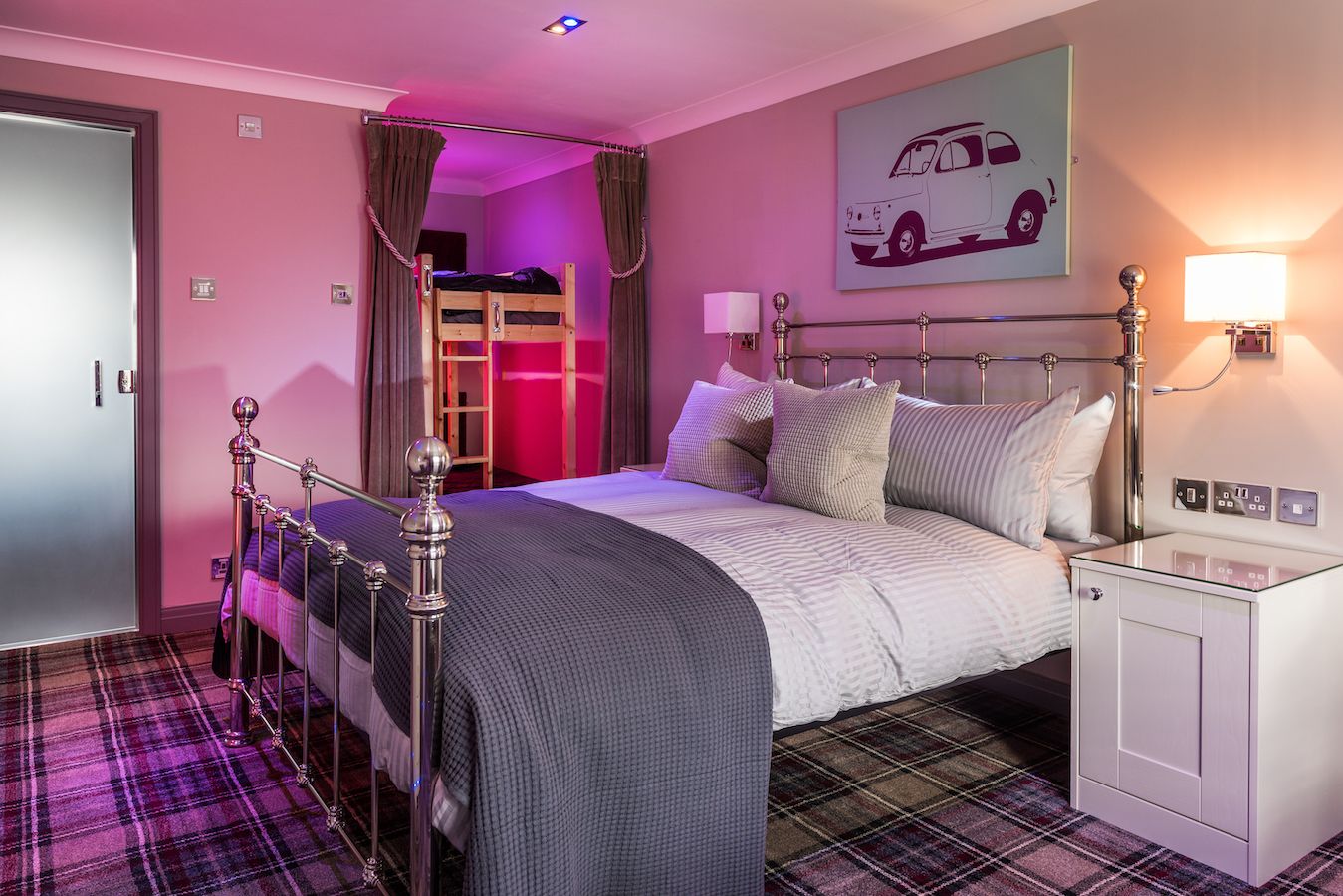 A bedroom with a bunk bed, a bedside table with a lamp, a wardrobe, and a car-themed wall art.