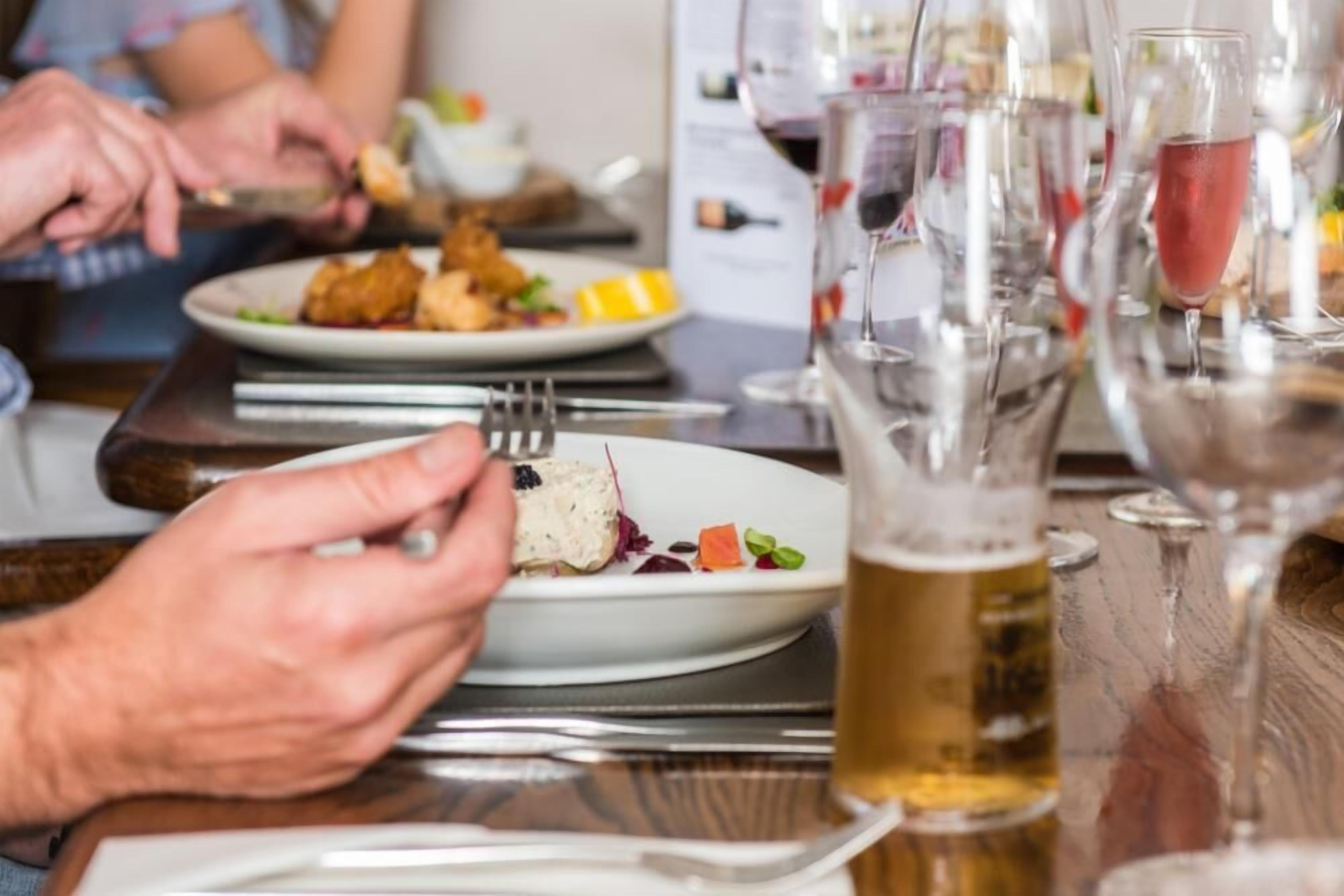 A dining table with plates of food, glasses of beer, and a person eating.