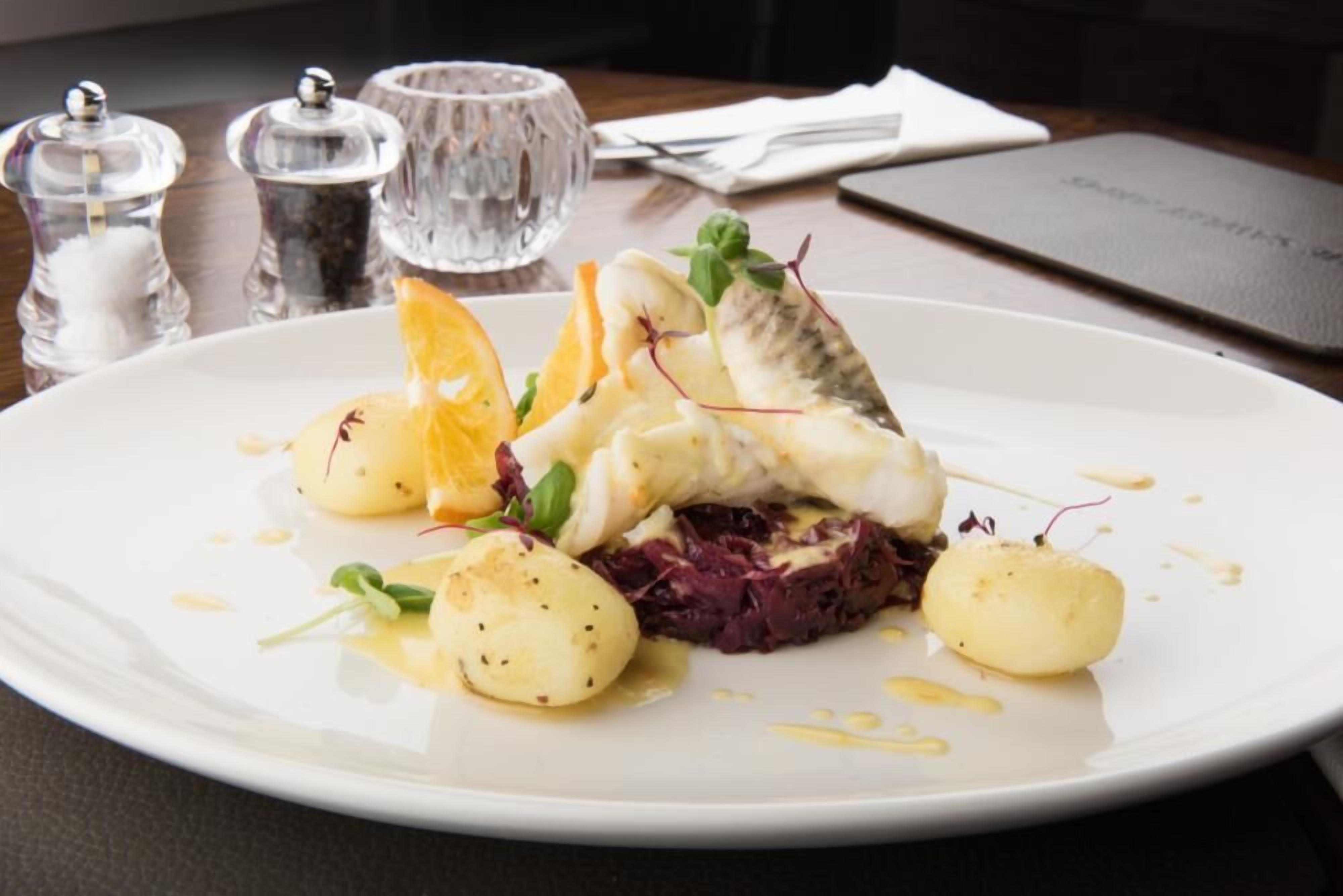Un plato blanco con un filete de pescado, patatas y col roja sobre una mesa.