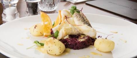 Un plato blanco con un filete de pescado, patatas y col roja sobre una mesa.