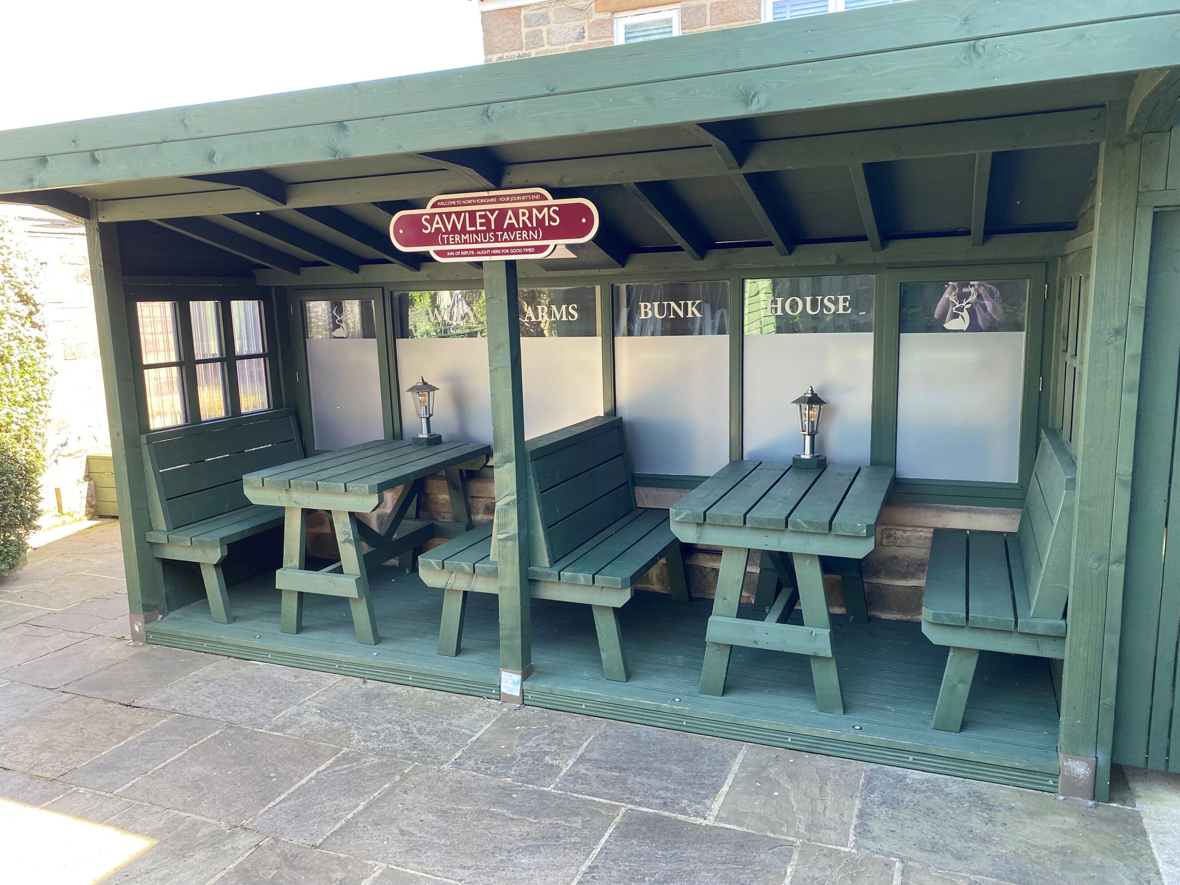 A covered outdoor seating area with wooden benches and tables, a sign reading "Sawley Arms (Terminus Tavern)," and a wall with partially visible text.
