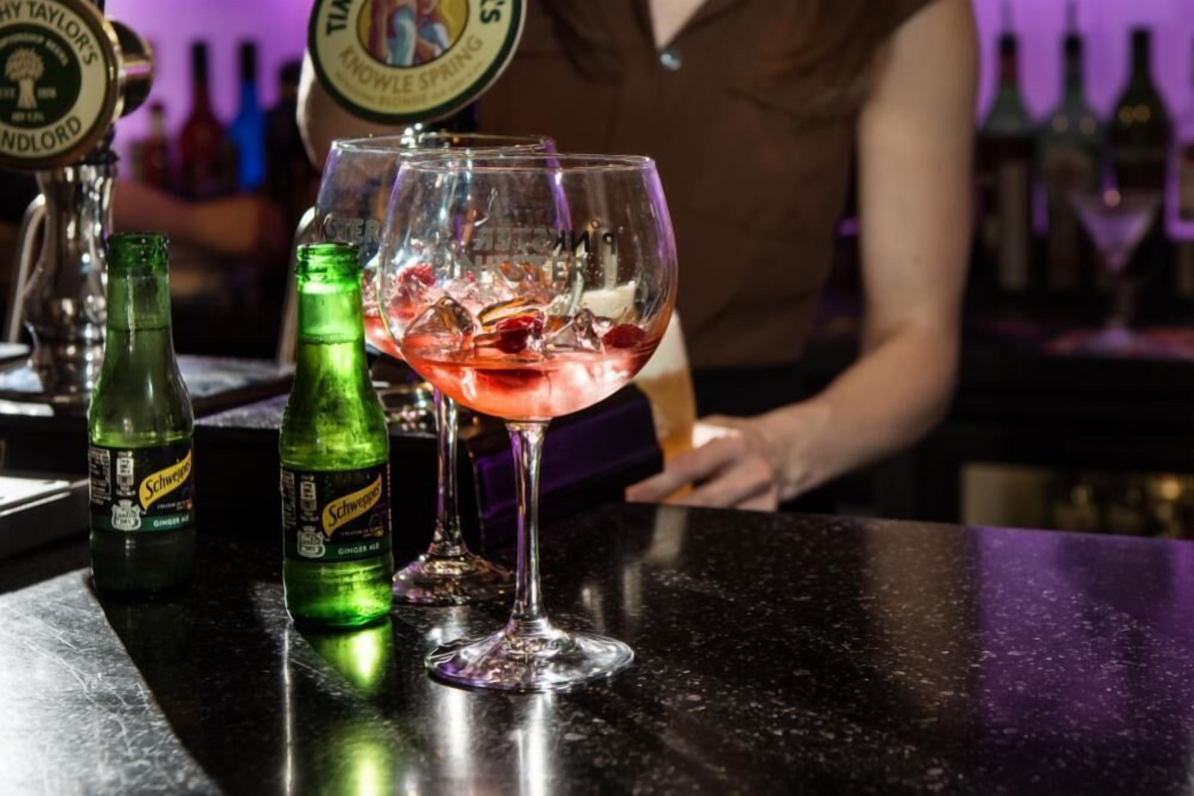 A bar setting with a drink in a glass, a bottle of Schweppes ginger ale, and a tap labeled 'Timothy Taylor's Knowles Spring'.