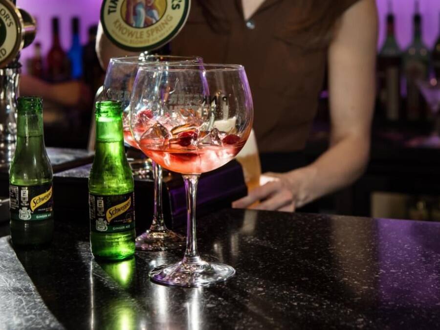A bar setting with a drink in a glass, a bottle of Schweppes ginger ale, and a tap labeled 'Timothy Taylor's Knowles Spring'.