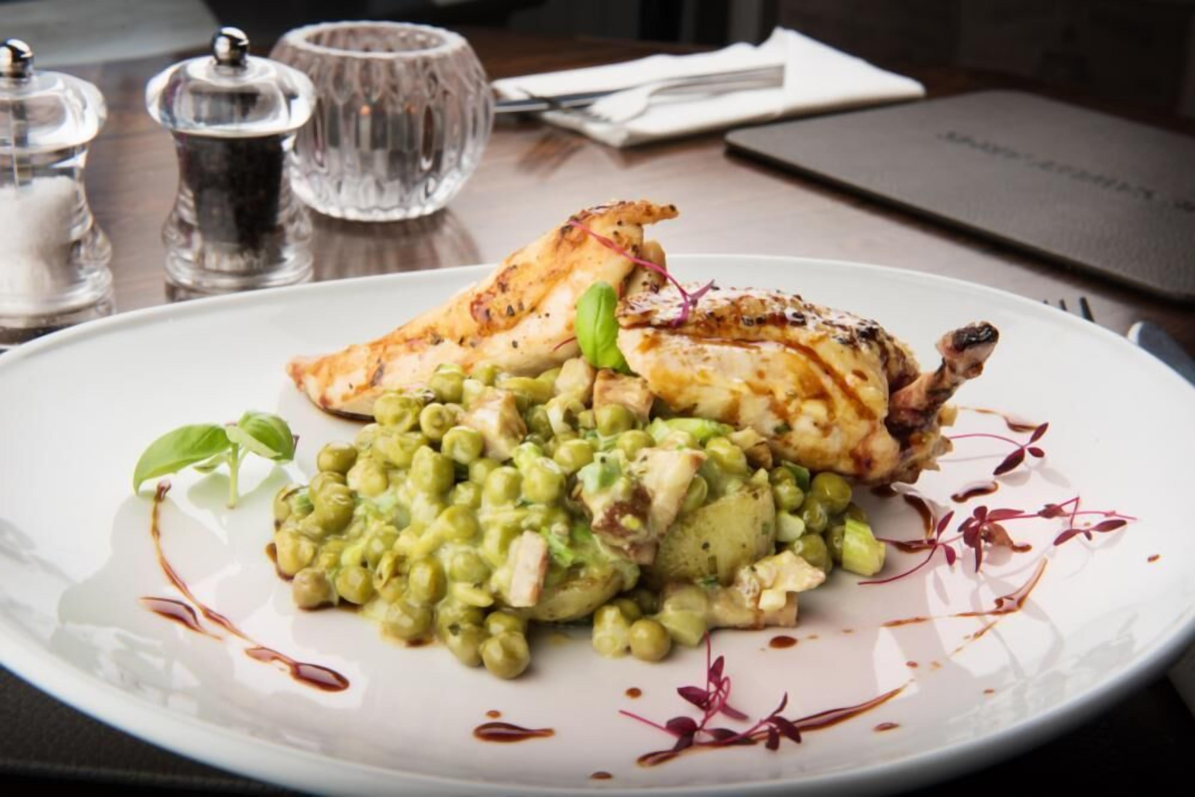 A plate of food with a grilled chicken leg, peas, and a creamy sauce, served on a white plate.