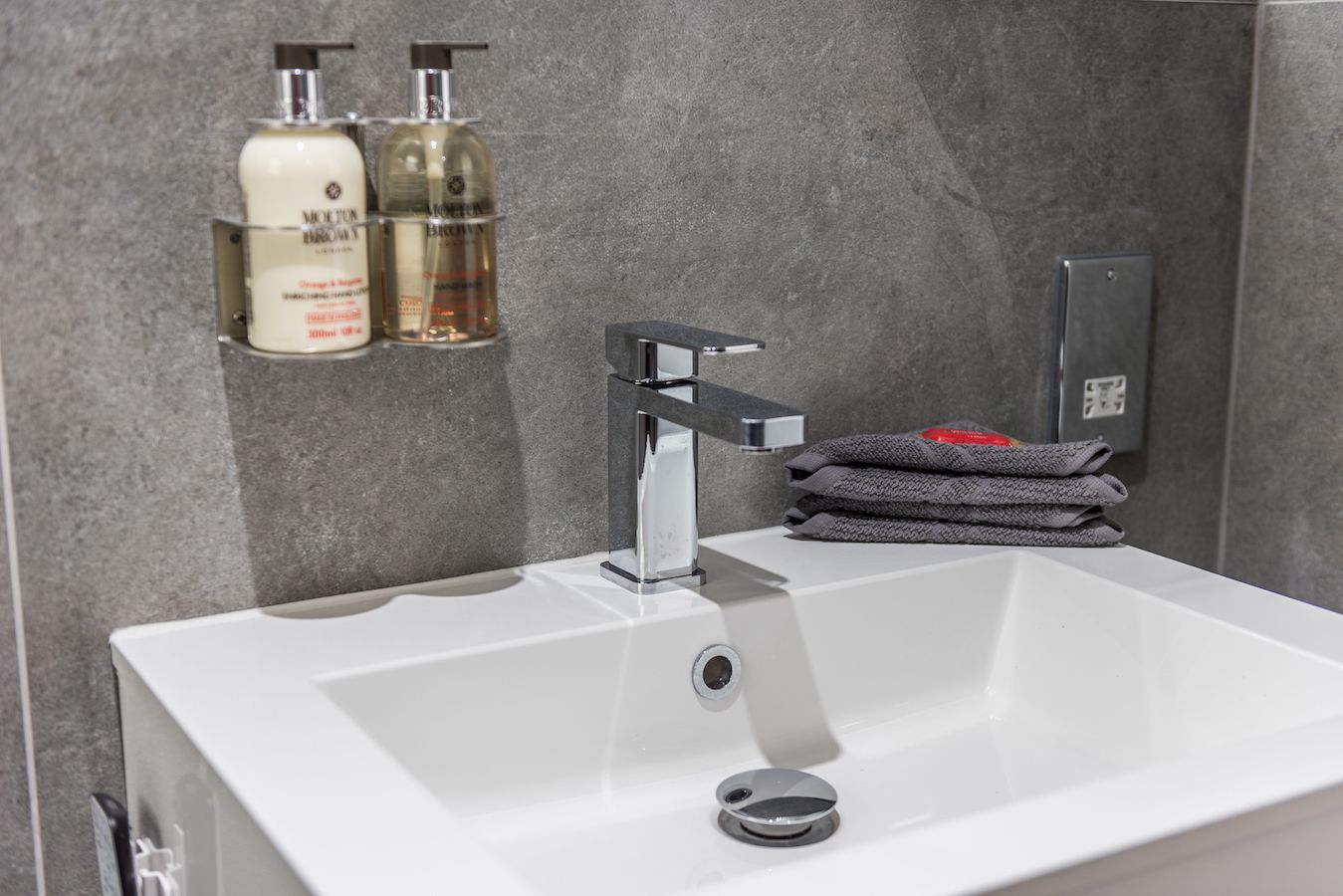 Une salle de bain moderne avec un lavabo blanc, un robinet chromé et deux flacons de produits de toilette posés sur une étagère.