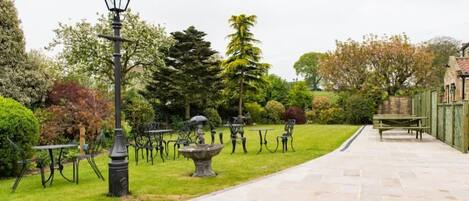 Un jardin avec des allées pavées de pierres, des tables et des chaises en métal, et un lampadaire.
