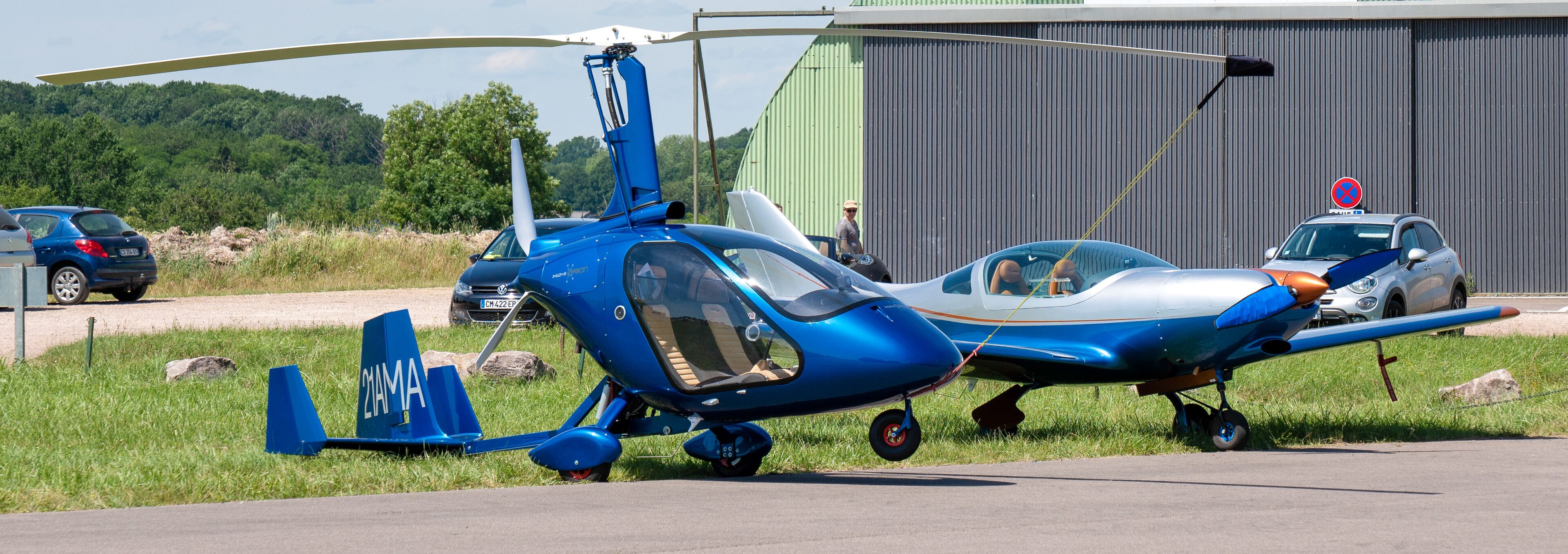 A blue helicopter and a small airplane parked on a grassy area near a building.