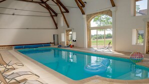 Una piscina interior con agua azul cristalina, rodeada de suelo de baldosas y vigas de madera.
