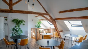 Un interior moderno con vigas de madera, mesas redondas y sillas anaranjadas.